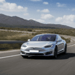 Silver Tesla Model S driving on a scenic highway, illustrating the promise of autonomous technology versus real-world road conditions.