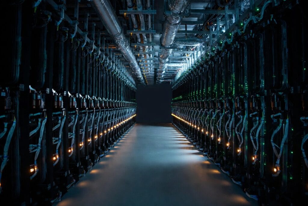 A wide-angle interior view of a massive AI Infrastructure data centre aisle lined with rows of dark, industrial server racks illuminated by rhythmic status lights, highlighting the scale and complexity of AI hardware